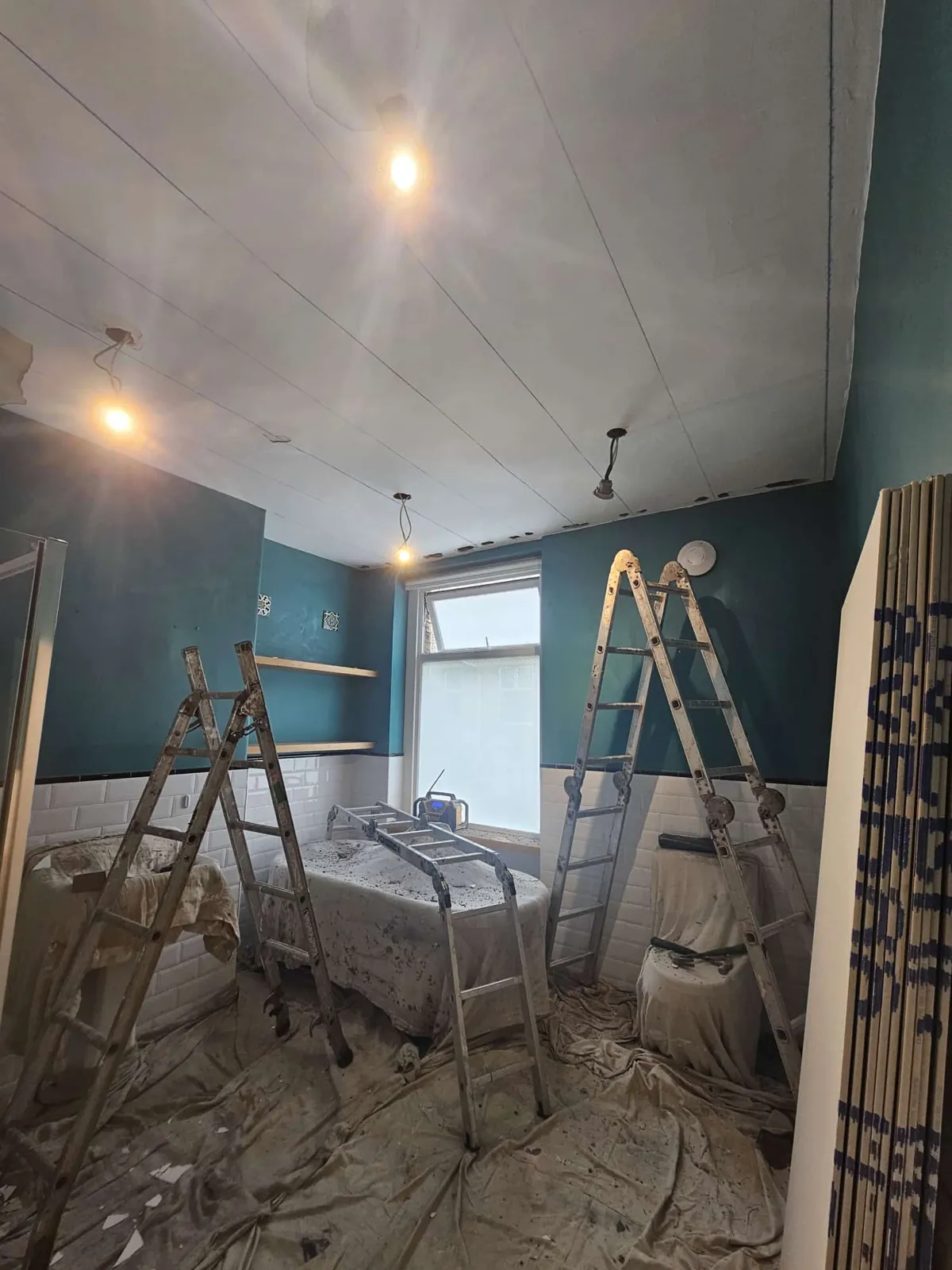 Bathroom ceiling newly plasterboarded with stepladders and dust sheets covering the bath and floor