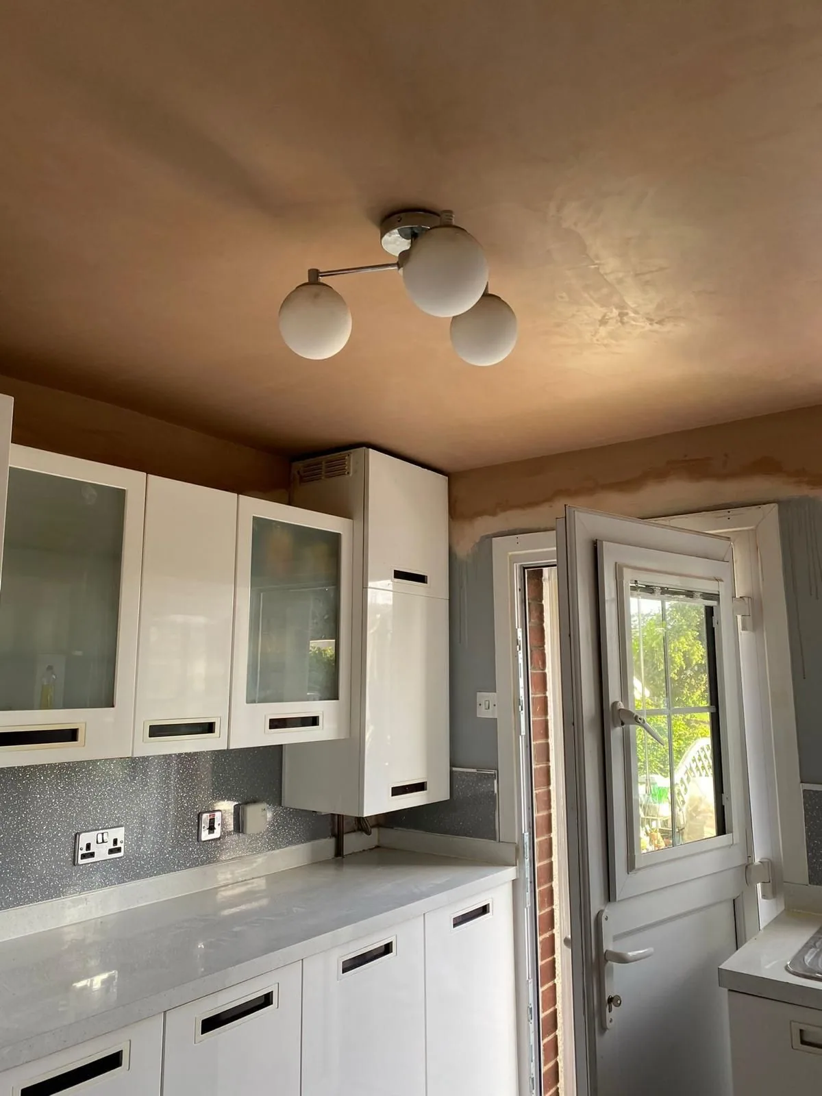 Kitchen with a freshly skimmed pink plaster ceiling drying above existing units