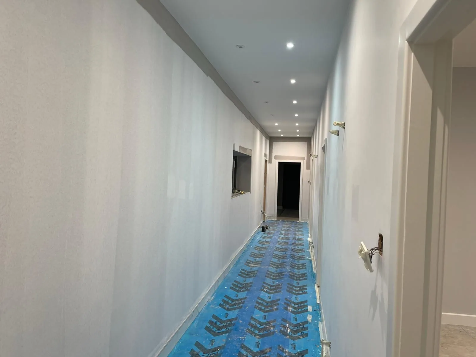 Long corridor walls freshly plastered, drying before paint, with floor protection laid down